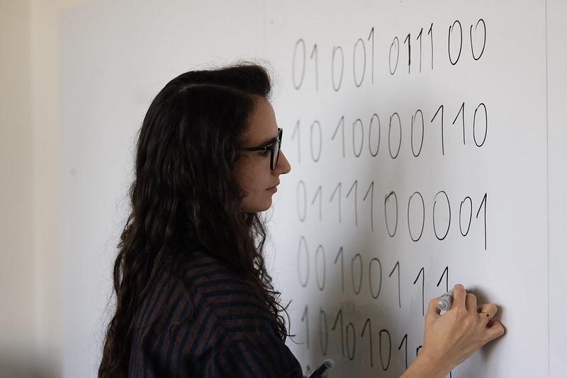 Une étudiante rédige au tableau blanc des lignes de codes binaires